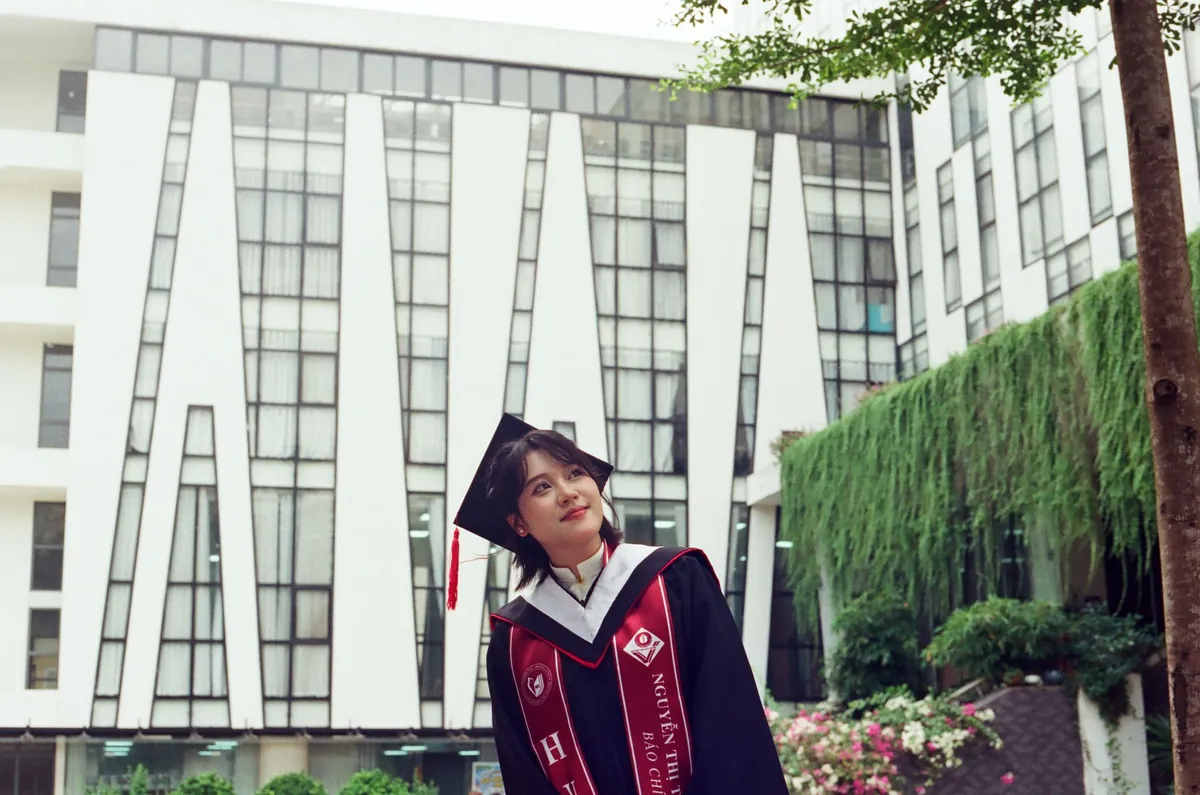 身穿学士服的年轻女性在户外现代建筑前微笑留影。